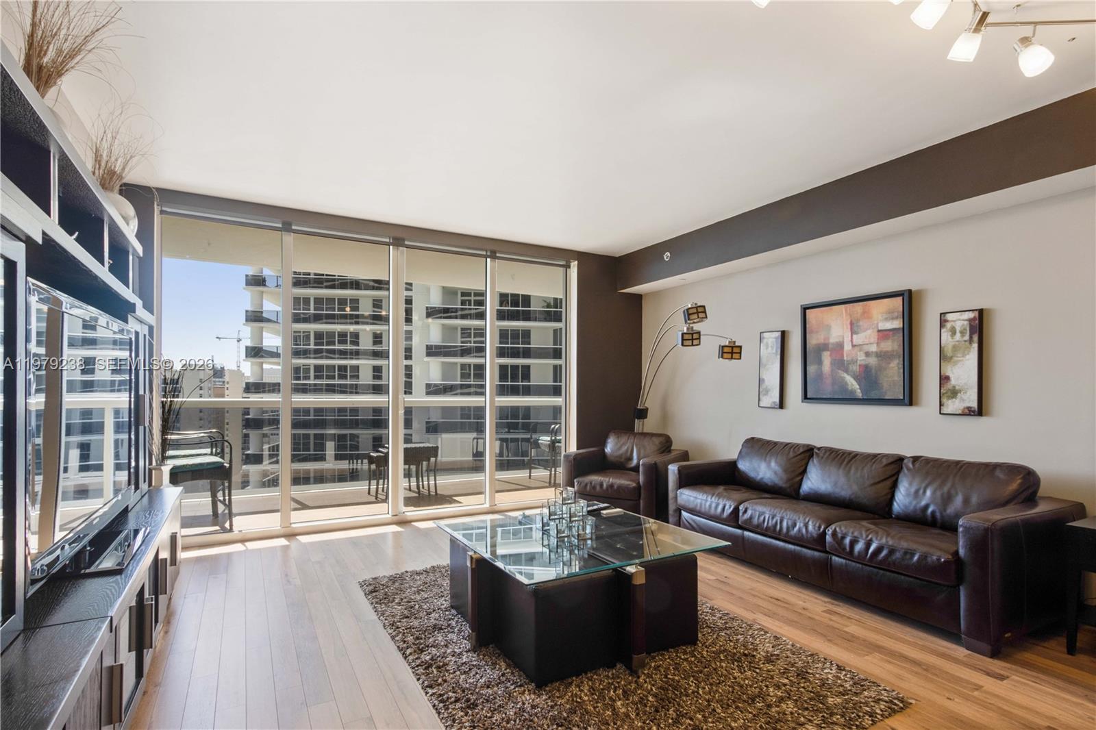 A living room features a brown leather sofa, glass coffee table, and floor-to-ceiling windows — 1830 S Ocean Dr # 2105, Hallandale Beach FL 33009, HALLANDALE BEACH, FL