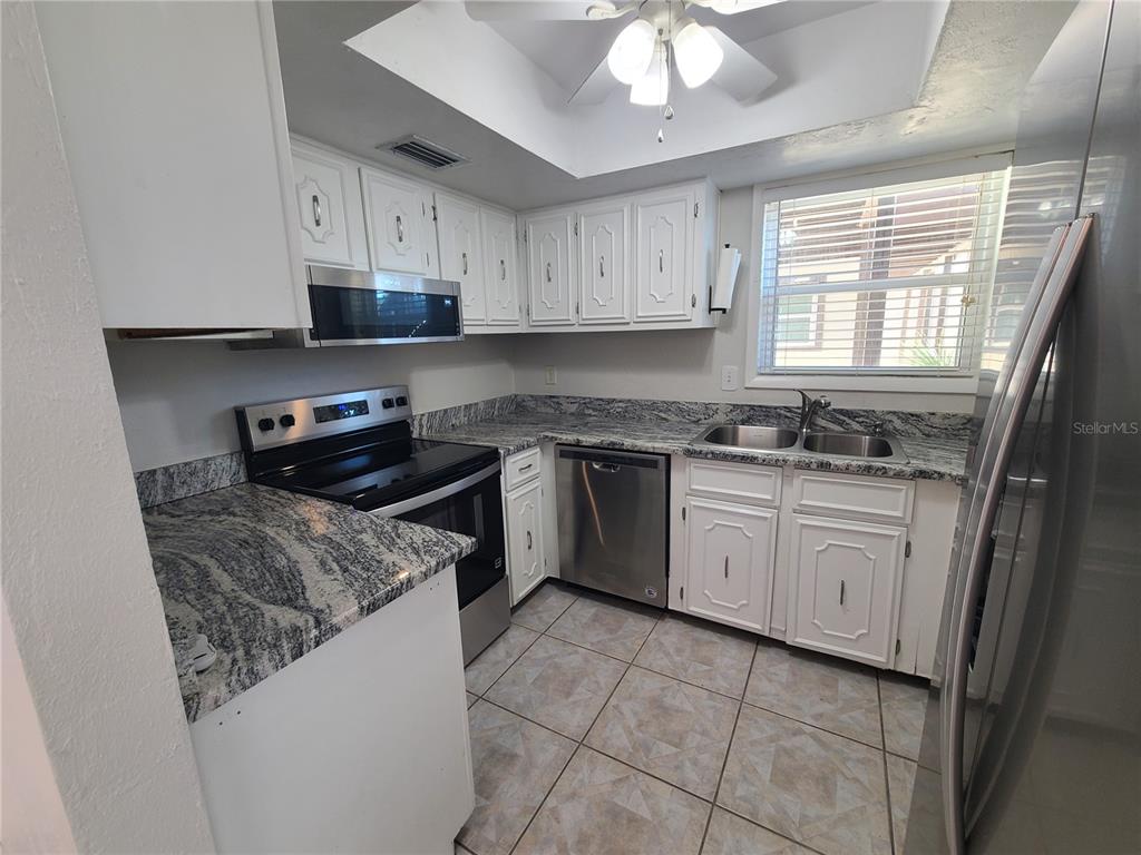 A kitchen features white cabinets, granite countertops, stainless steel appliances, and tiled flooring — 18101 SANDALWOOD DRIVE, WILDWOOD, FL