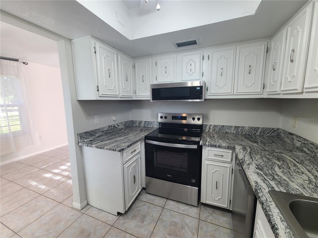 A kitchen features white cabinets, granite countertops, and stainless steel appliances — 18101 SANDALWOOD DRIVE, WILDWOOD, FL