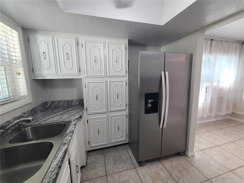A kitchen features white cabinets, granite countertops, a stainless steel refrigerator, and tile flooring — 18101 SANDALWOOD DRIVE, WILDWOOD, FL