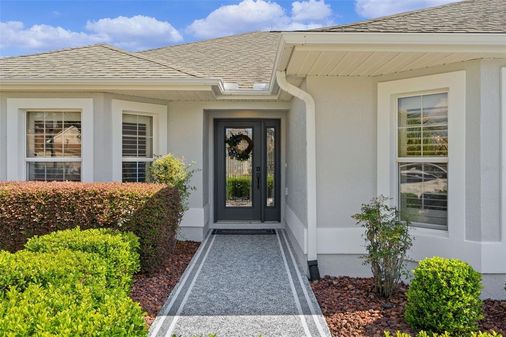 The exterior of a house features a gray front door, a stone walkway, and landscaping — 634 ALLENWOOD LOOP, THE VILLAGES, FL