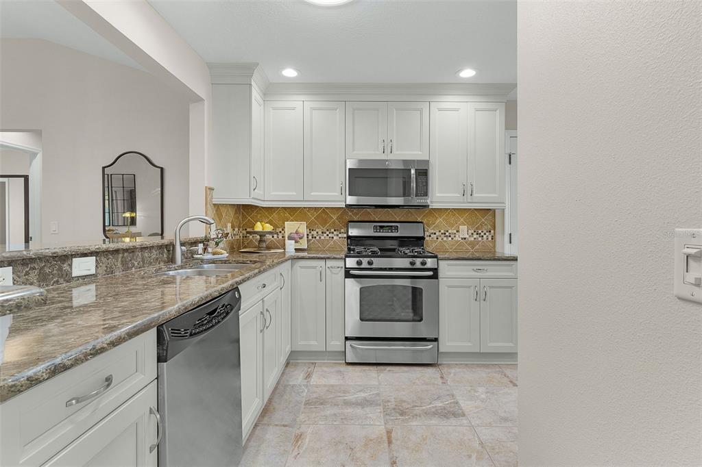 A kitchen features white cabinets, granite countertops, stainless steel appliances, and a tiled backsplash — 634 ALLENWOOD LOOP, THE VILLAGES, FL