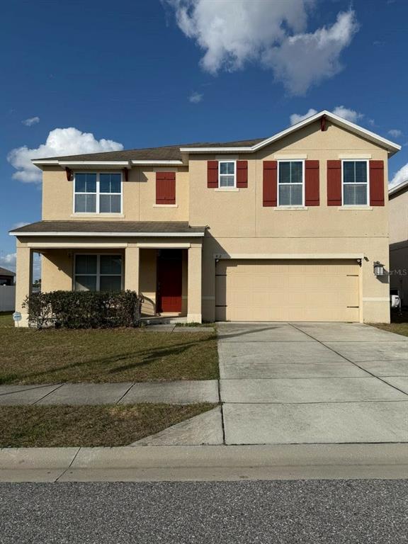 A two-story suburban house with tan stucco siding, red shutters, and a two-car garage — 412 NOVA DRIVE, DAVENPORT, FL