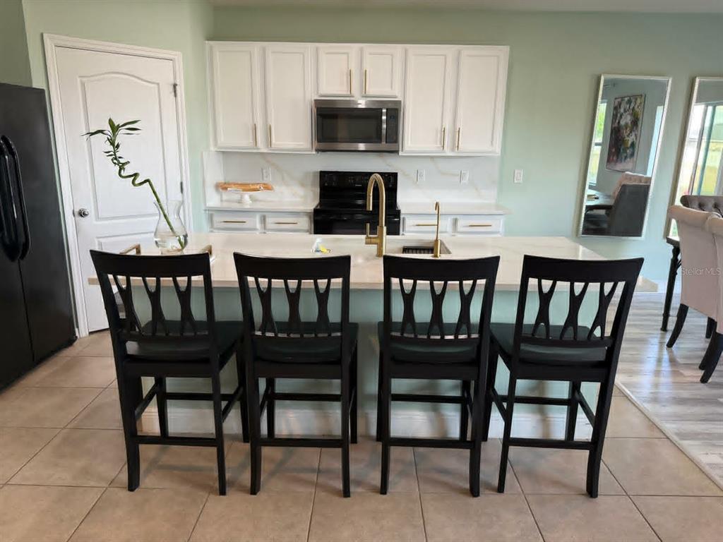 A kitchen features white cabinets, a central island with four black chairs, and gold fixtures — 412 NOVA DRIVE, DAVENPORT, FL