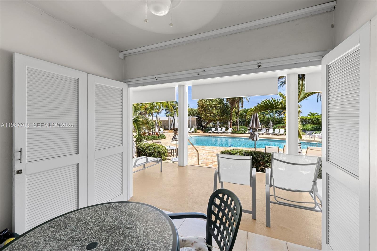 A patio with a table and chairs overlooks a swimming pool through open doors — 5055 Collins Ave, Miami Beach FL 33140, MIAMI BEACH, FL