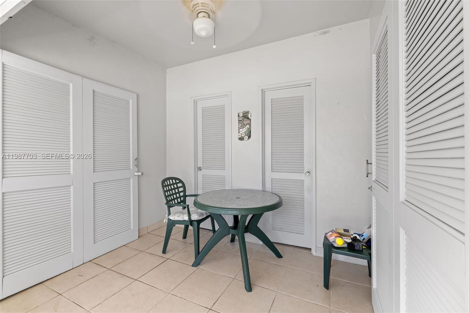 A small, tiled room features a round table, one chair, and several louvered closet doors — 5055 Collins Ave, Miami Beach FL 33140, MIAMI BEACH, FL