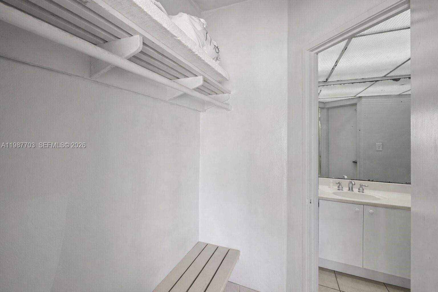 A small white closet with a slatted shelf and bench leads into a bathroom — 5055 Collins Ave, Miami Beach FL 33140, MIAMI BEACH, FL