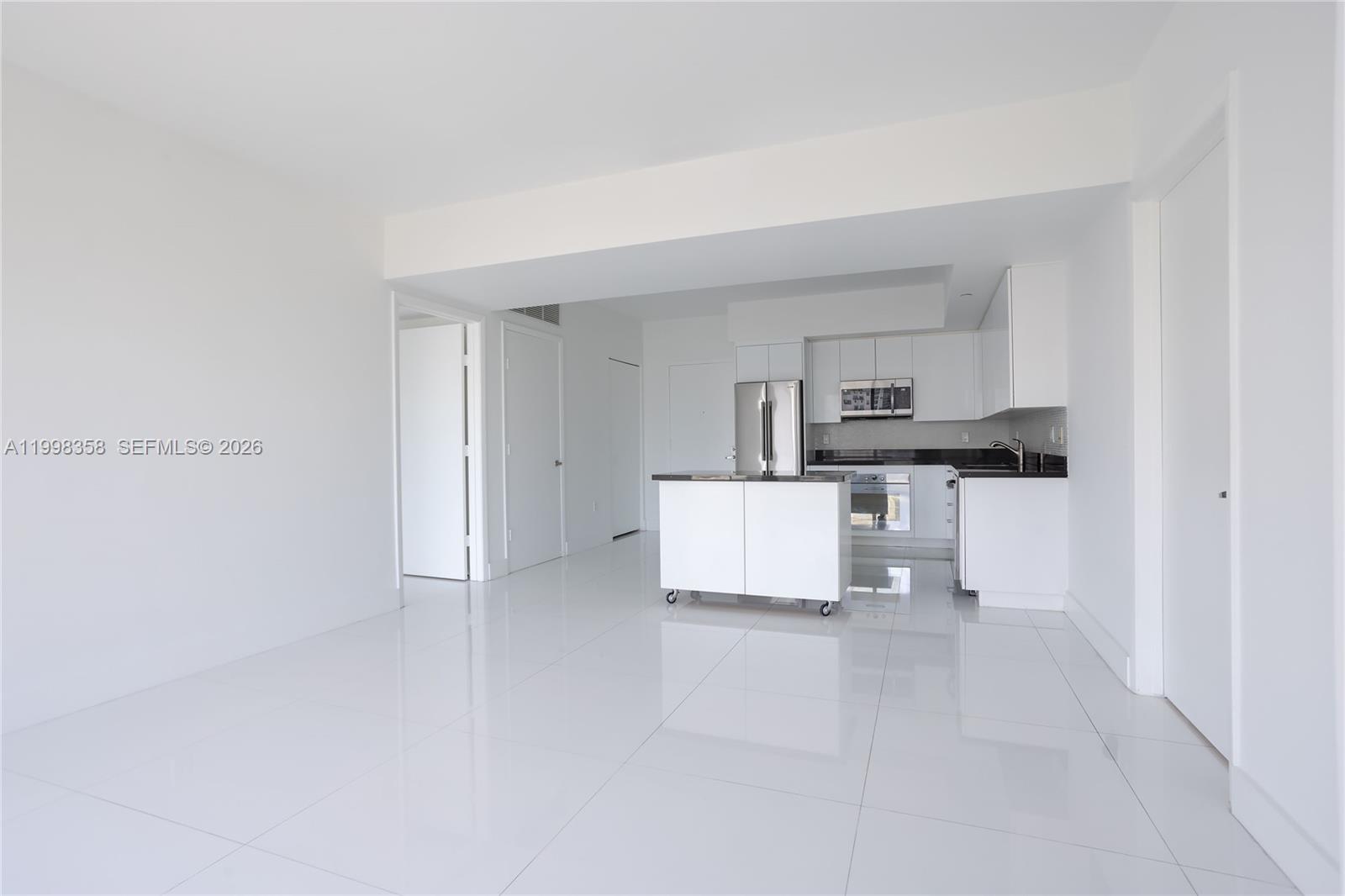 A minimalist kitchen with white cabinetry and a portable island sits in an open-plan room — 92 SW 3rd St # 3512, Miami FL 33130, MIAMI, FL