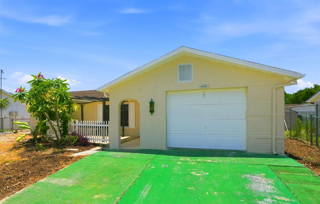 A single-story house with a white garage door, a green driveway, and a small porch — 6430 BALDWYN AVENUE, NEW PORT RICHEY, FL