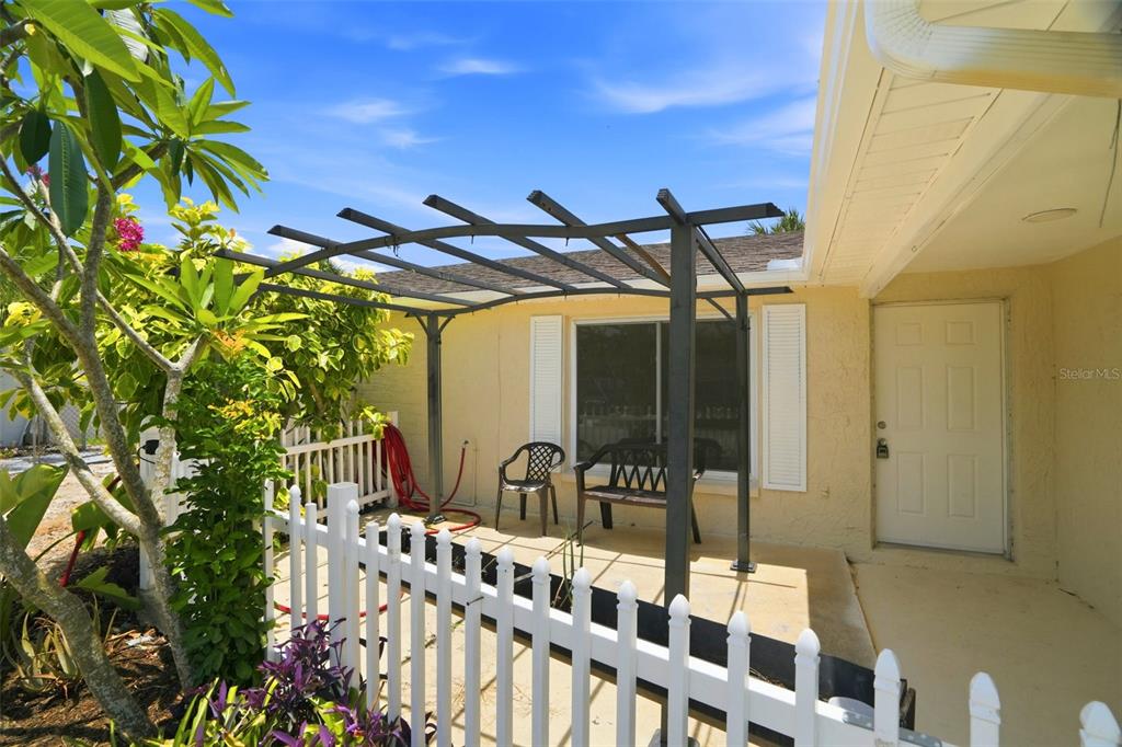 A patio with a metal pergola, a white picket fence, and a door to the house — 6430 BALDWYN AVENUE, NEW PORT RICHEY, FL