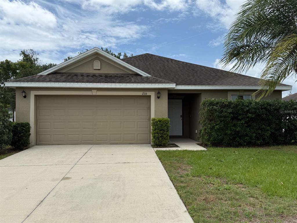 A single-story house with a tan stucco exterior, a two-car garage, and a shingled roof — 235 ELEUTHERA DRIVE, LAKE ALFRED, FL