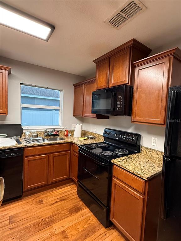 A kitchen features wood cabinets, granite countertops, black appliances, and light wood flooring — 235 ELEUTHERA DRIVE, LAKE ALFRED, FL