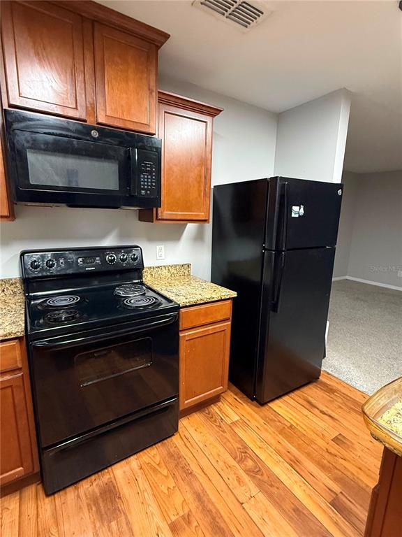 A kitchen features wooden cabinets, granite countertops, and black appliances on a hardwood floor — 235 ELEUTHERA DRIVE, LAKE ALFRED, FL