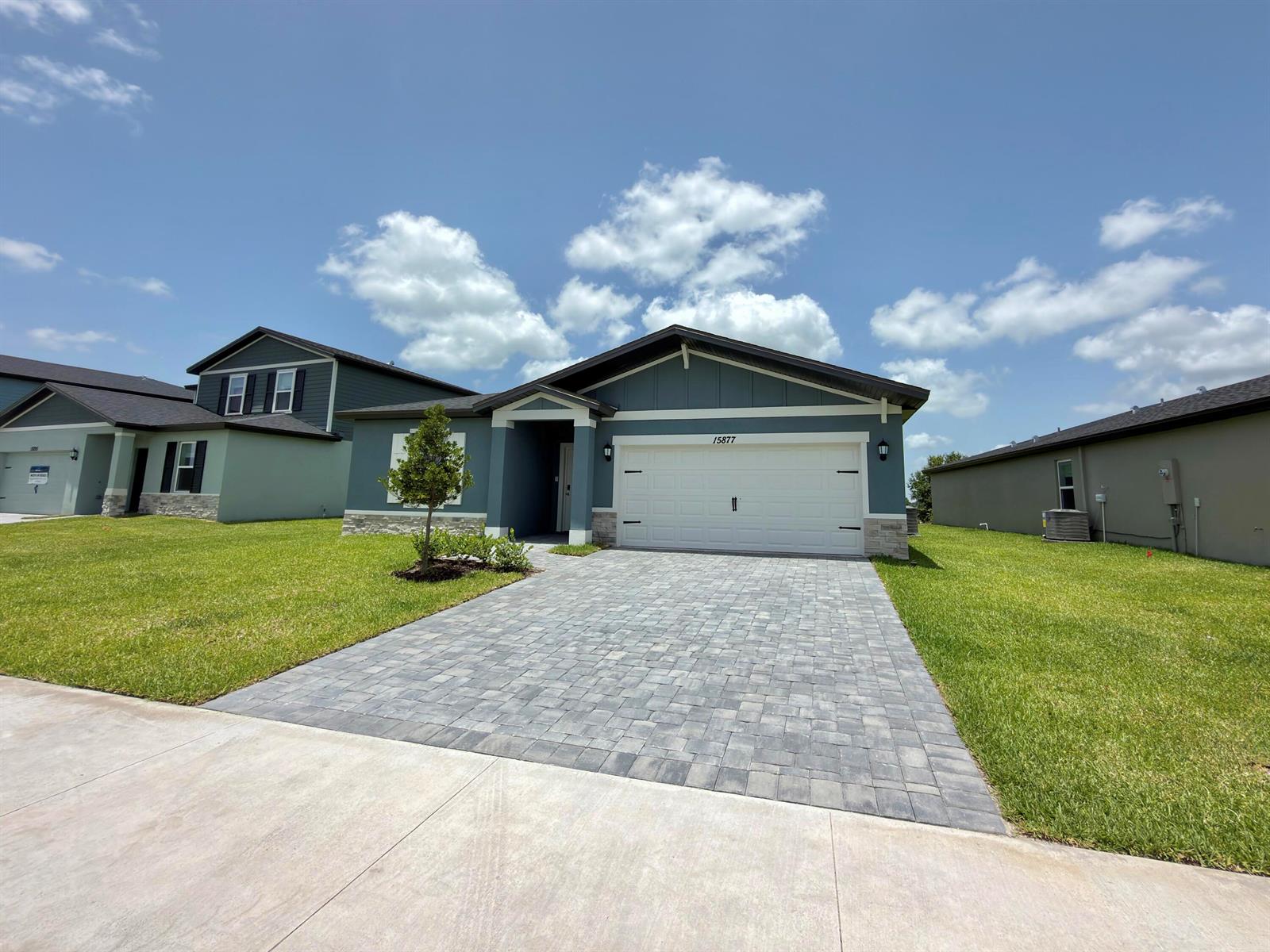 A blue single-story house features a white garage door and a paved driveway — 15877 SW Vine Drive, FL 34956, FL