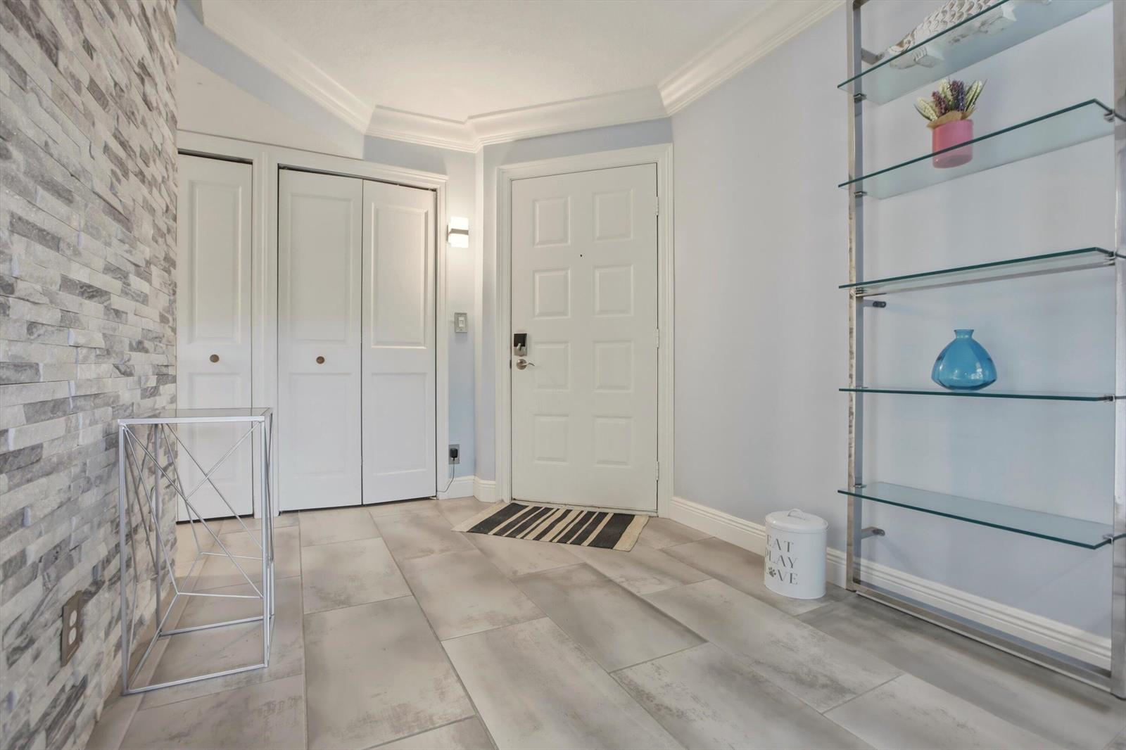 An entryway features light gray tile flooring, a white front door, and a glass shelving unit — 1605 S Us Highway 1 # C104, Jupiter FL 33477, JUPITER, FL