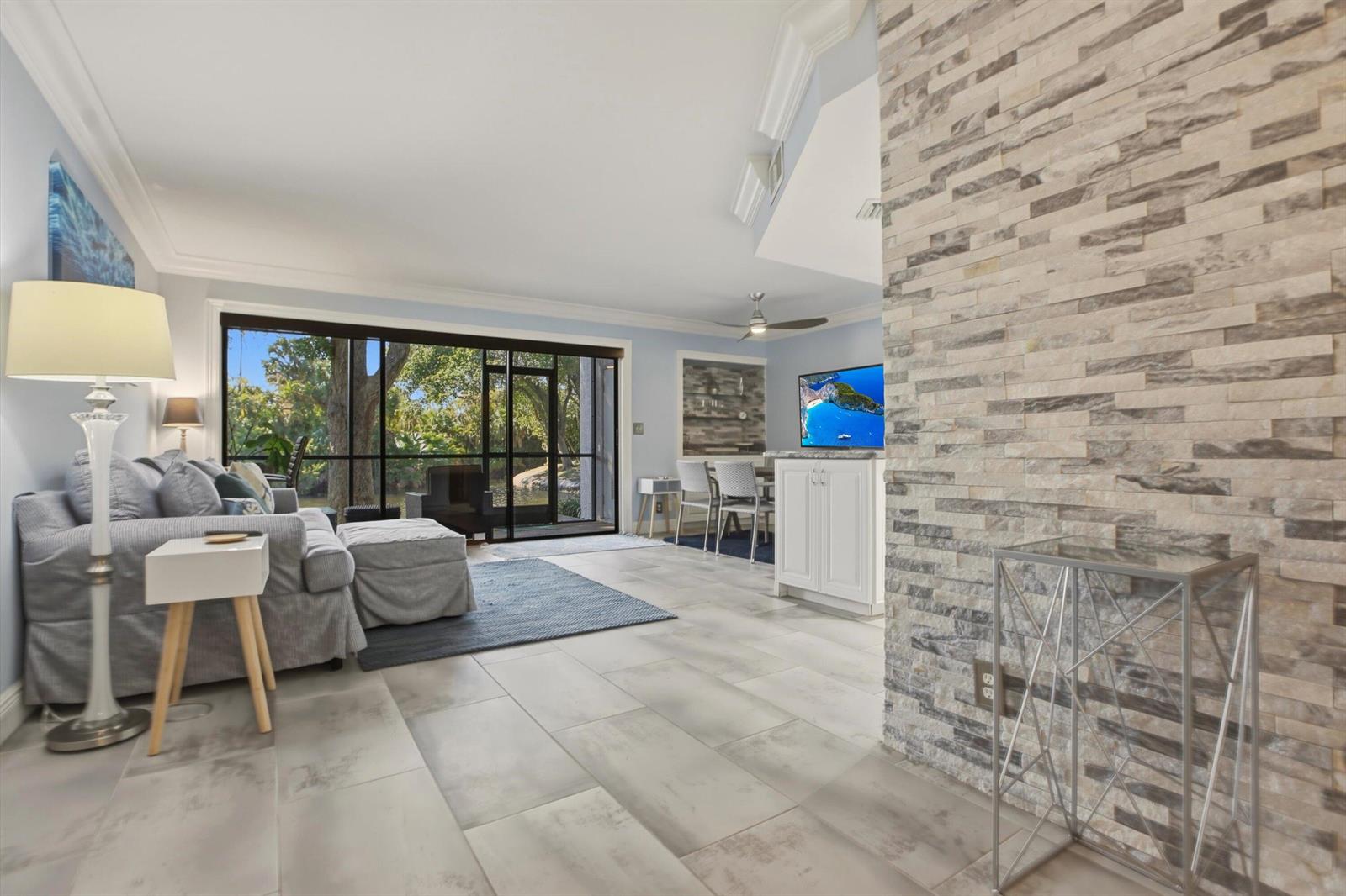 A living room features a stone accent wall, tile flooring, and a large sliding glass door — 1605 S Us Highway 1 # C104, Jupiter FL 33477, JUPITER, FL