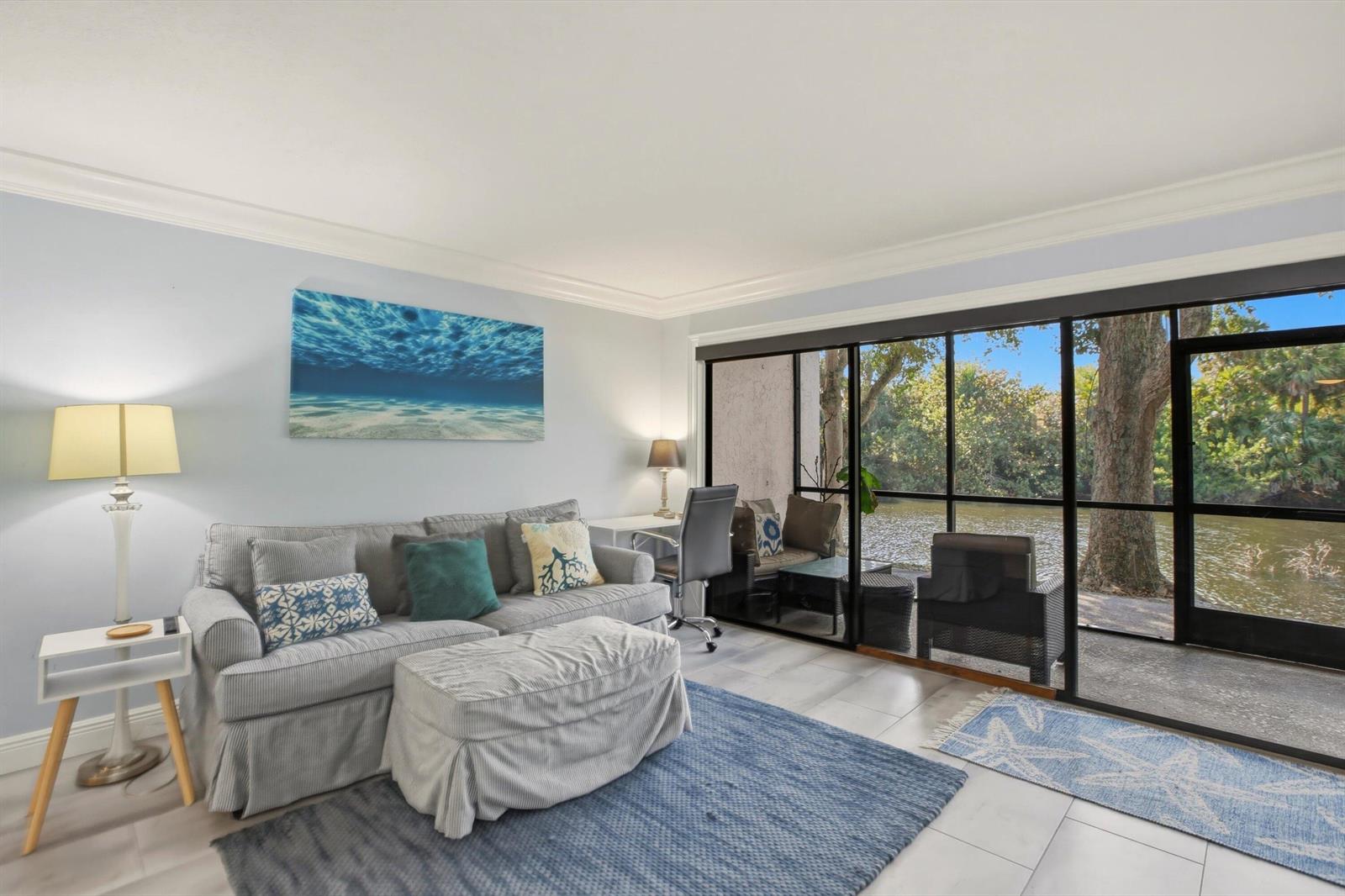 A living room features a gray sofa, blue rug, and sliding glass doors overlooking water — 1605 S Us Highway 1 # C104, Jupiter FL 33477, JUPITER, FL
