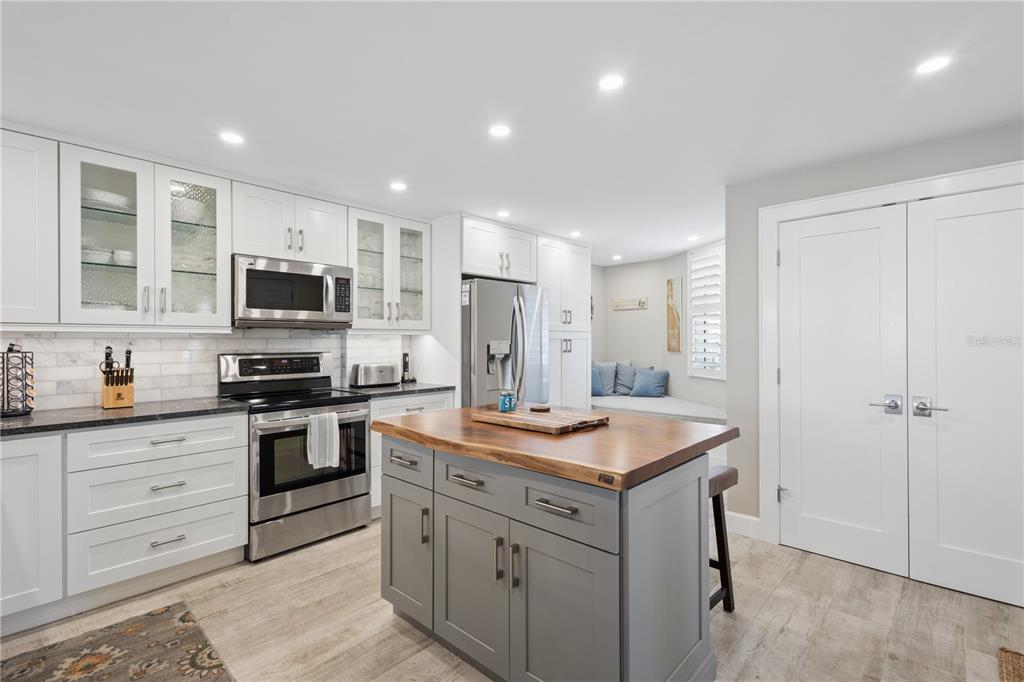A kitchen features white cabinets, a gray island with a wood countertop, and stainless appliances — 5880 MIDNIGHT PASS ROAD UNIT 704, SARASOTA, FL