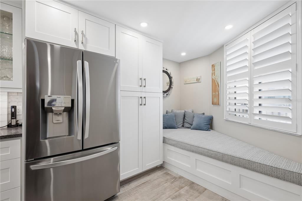 A kitchen features a stainless steel refrigerator, white cabinetry, and a built-in window seat — 5880 MIDNIGHT PASS ROAD UNIT 704, SARASOTA, FL