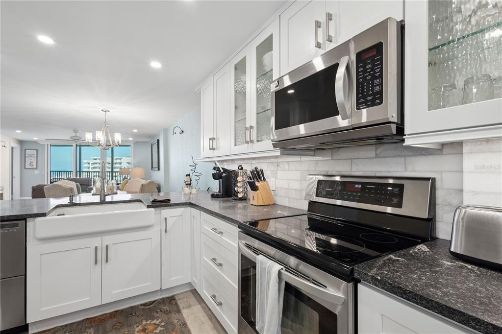 A kitchen features white cabinetry, dark countertops, stainless steel appliances, and a farmhouse sink — 5880 MIDNIGHT PASS ROAD UNIT 704, SARASOTA, FL