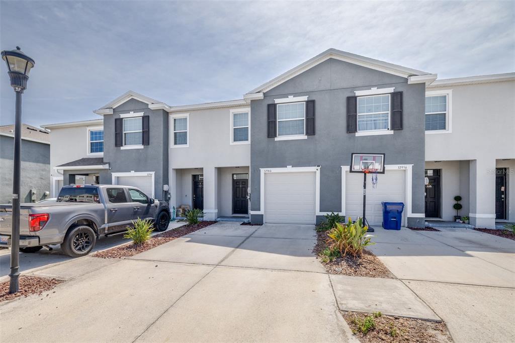 A row of two-story townhomes with gray and white facades, garages, and concrete driveways — 32960 KALOKO ROAD, WESLEY CHAPEL, FL