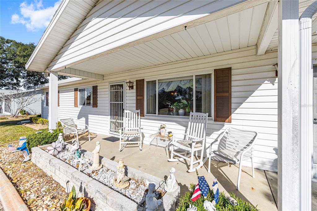 A white house exterior features a covered porch with rocking chairs and decorative garden statues — 10319 SE 177TH PLACE, SUMMERFIELD, FL