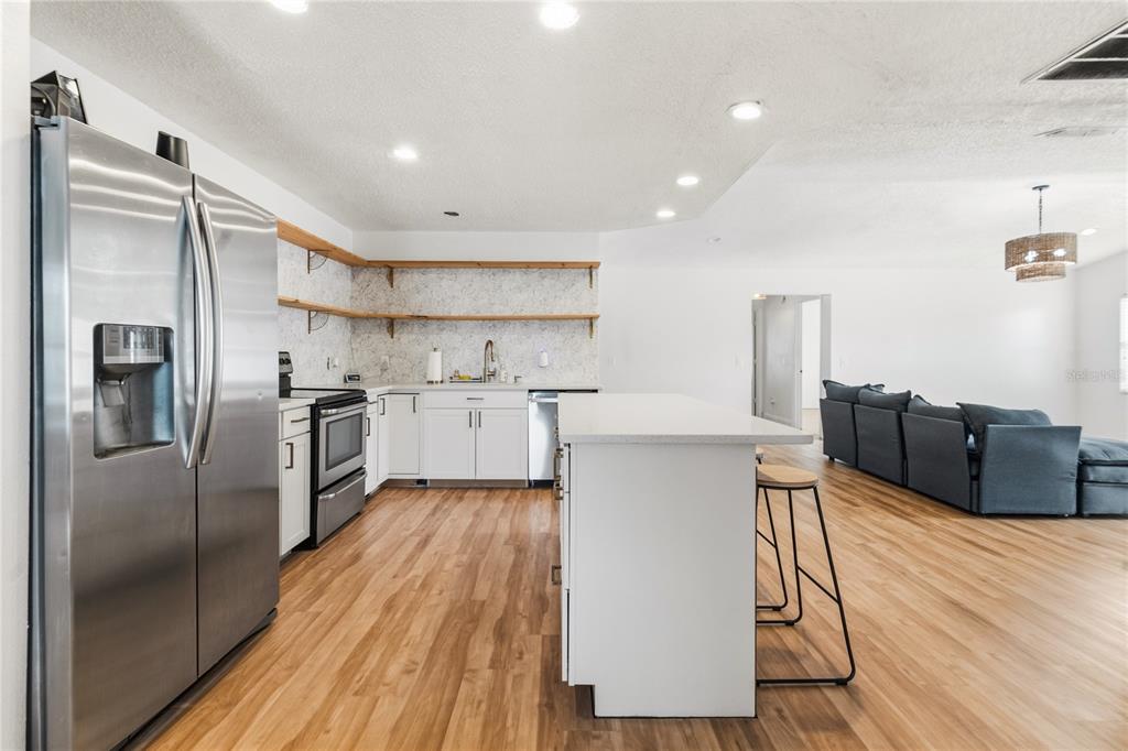 A modern kitchen with white cabinets, wood shelving, stainless steel appliances, and a central island — 352 VAIL DRIVE, WINTER HAVEN, FL