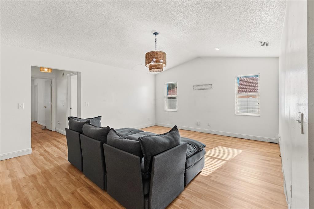 A living room features light wood flooring, white walls, a vaulted ceiling, and a grey sofa — 352 VAIL DRIVE, WINTER HAVEN, FL