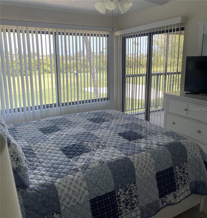 A bedroom features a blue and white patchwork quilt, vertical blinds, and a sliding door — 6343 PALMA DEL MAR BOULEVARD S UNIT 226, ST PETERSBURG, FL