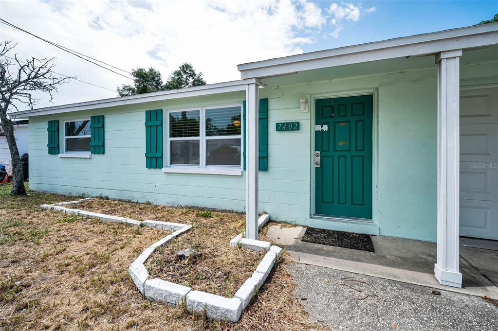 A light green house exterior features a dark green front door and teal window shutters — 7402 COUNTRY CLUB DRIVE, HUDSON, FL