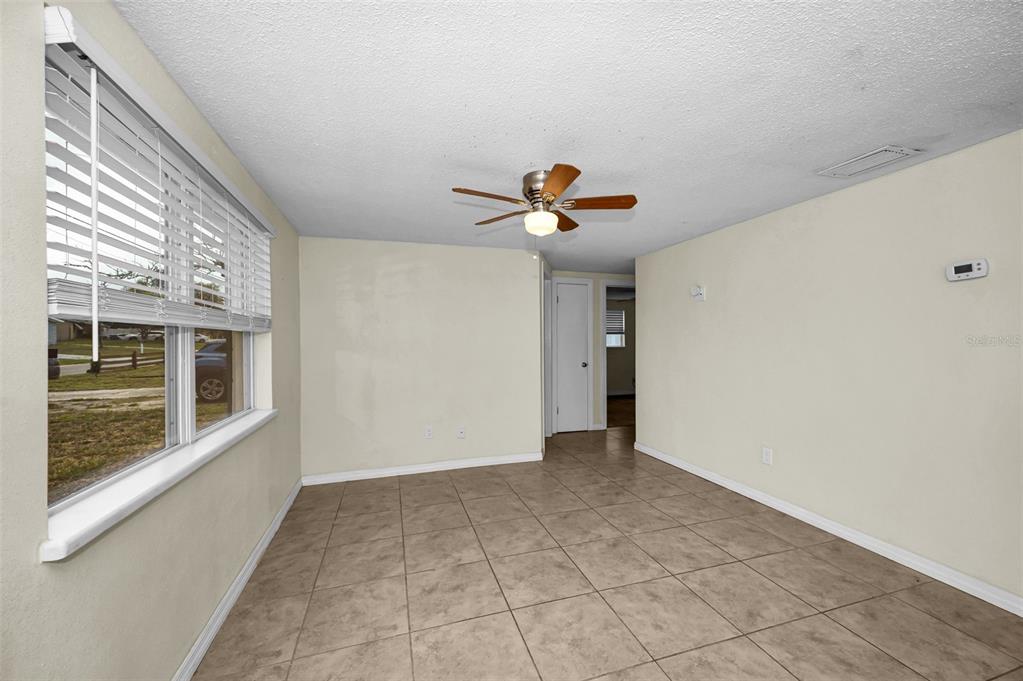 A room with beige walls, tan tile flooring, a ceiling fan, and a large window — 7402 COUNTRY CLUB DRIVE, HUDSON, FL