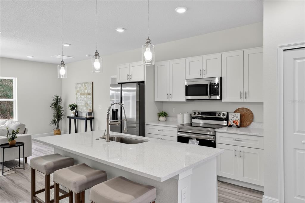 A modern kitchen features white cabinetry, stainless steel appliances, and a large quartz-topped island — 15742 SW 37TH CIRCLE, OCALA, FL