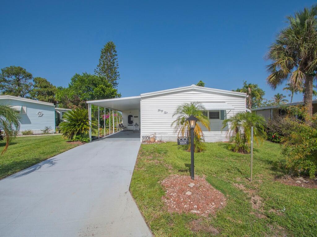 A white mobile home features a carport, a concrete driveway, and a landscaped front yard — 42 Village Lane, Jensen Beach FL 34957, JENSEN BEACH, FL
