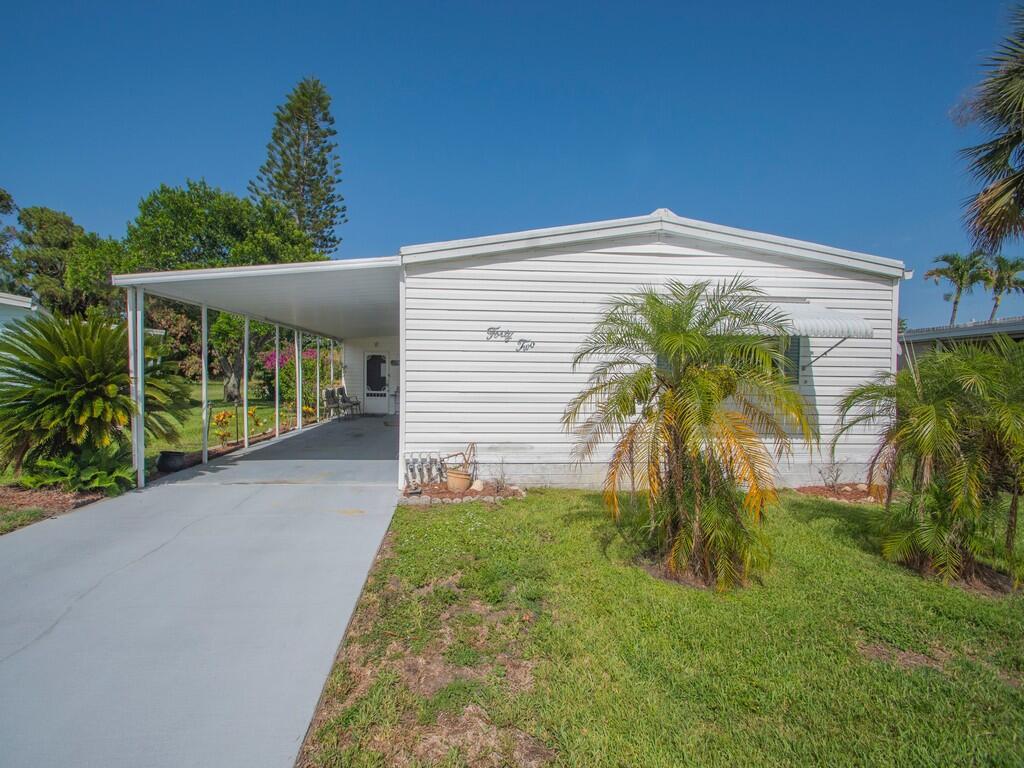 A white mobile home with a carport and a palm tree in the front yard — 42 Village Lane, Jensen Beach FL 34957, JENSEN BEACH, FL