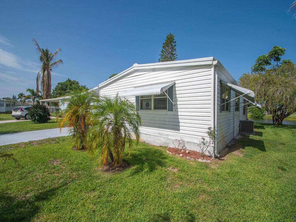 A white mobile home with horizontal siding and metal window awnings sits on a lawn — 42 Village Lane, Jensen Beach FL 34957, JENSEN BEACH, FL