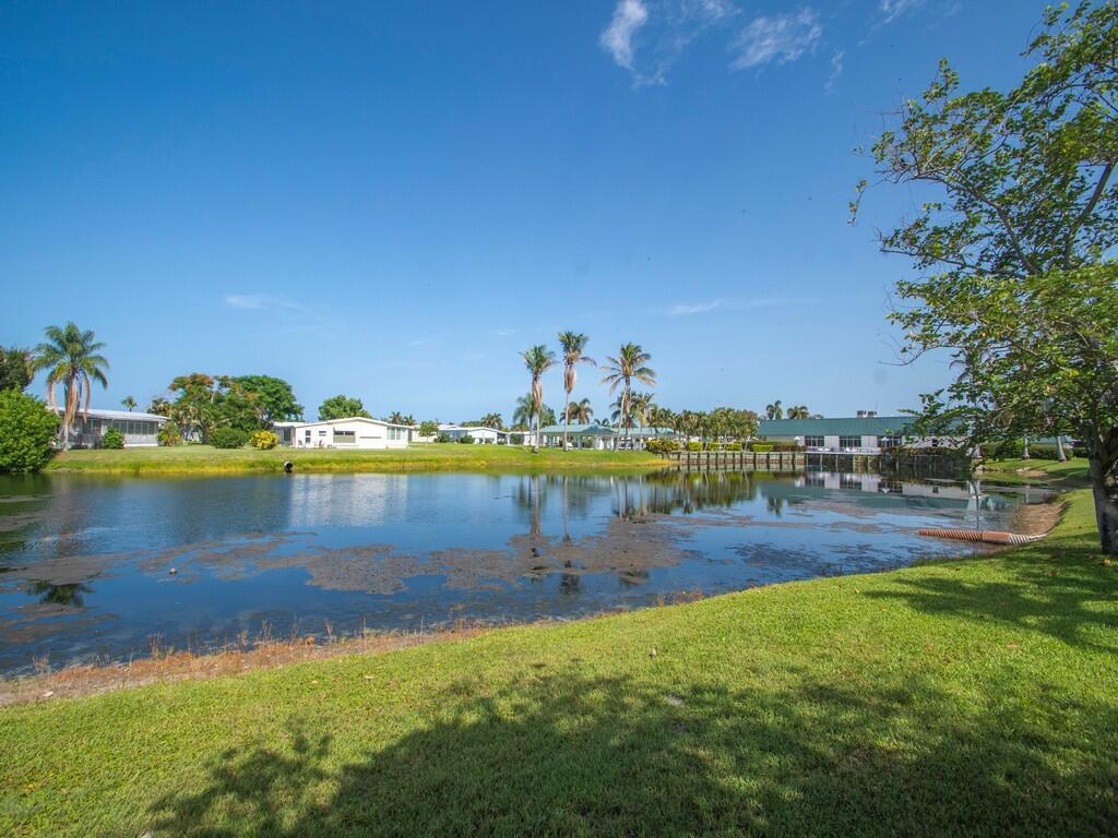 A grassy yard overlooks a pond with houses and palm trees in the background — 42 Village Lane, Jensen Beach FL 34957, JENSEN BEACH, FL