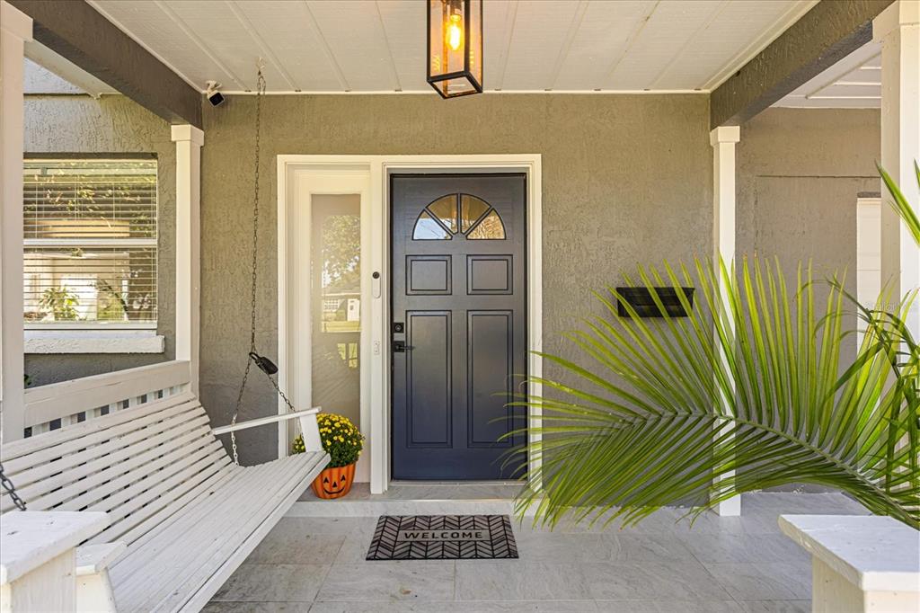 A covered porch features a white hanging bench, a dark blue front door, and a plant — 2418 EUSTON ROAD, WINTER PARK, FL