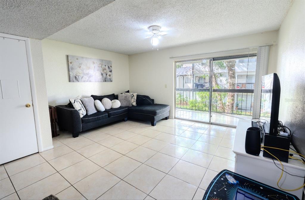 A living room features a dark sectional sofa, tile flooring, and a sliding glass balcony door — 4267 S SEMORAN BOULEVARD UNIT 11, ORLANDO, FL