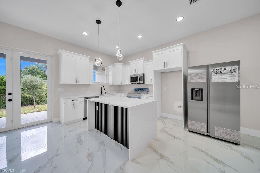 A modern kitchen features white cabinetry, a slatted island, stainless steel appliances, and marble flooring — 4648/4650 LEONARD BOULEVARD S, LEHIGH ACRES, FL