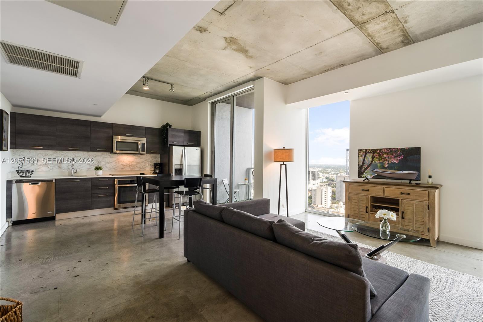A modern open-concept living area features a kitchen, gray sofa, and floor-to-ceiling windows — 151 SE 1st St # 3408, Miami FL 33131, MIAMI, FL