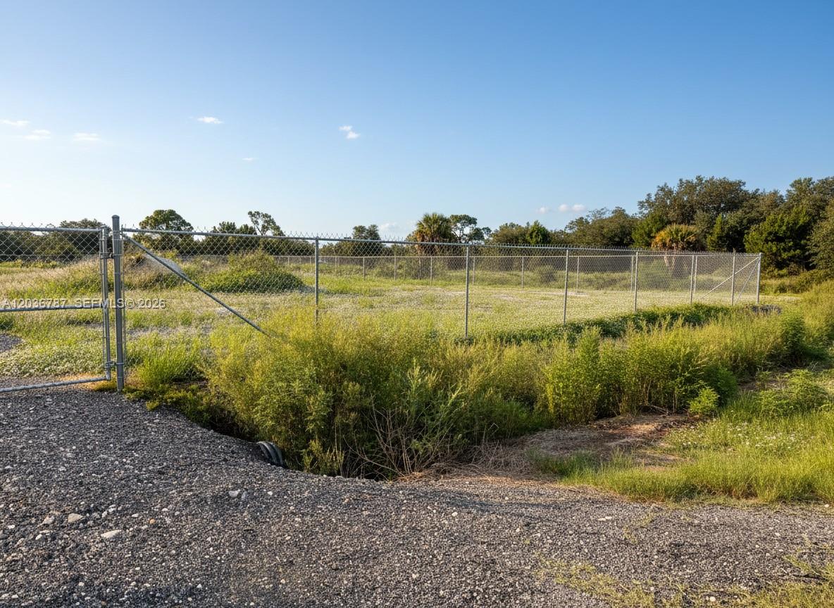 A fenced, grassy vacant lot with a gravel driveway entrance under a clear blue sky — 575 S JINETE ST, Clewiston FL 33440, CLEWISTON, FL