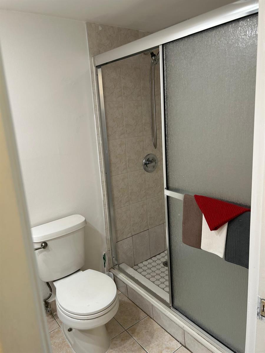A bathroom featuring a white toilet next to a glass-enclosed shower with tiled walls — 2661 S Course Drive # 703, Pompano Beach FL 33069, POMPANO BEACH, FL