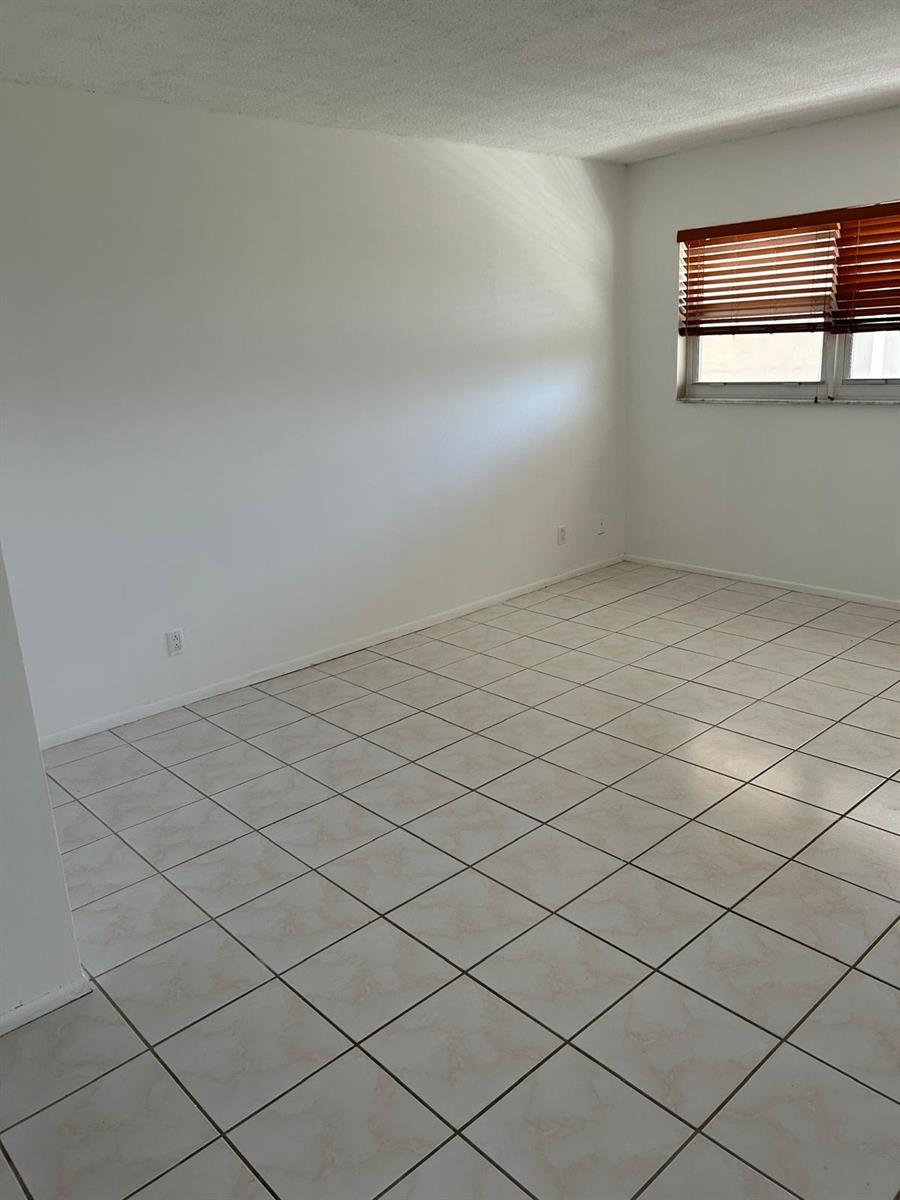 An empty room features white walls, a window with wooden blinds, and light-colored tiled flooring — 2661 S Course Drive # 703, Pompano Beach FL 33069, POMPANO BEACH, FL