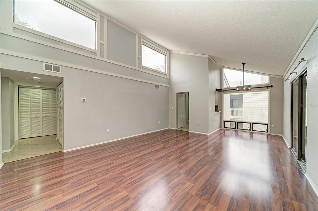 A living room with high vaulted ceilings, large windows, and dark wood-look laminate flooring — 2224 BAHIA VISTA STREET UNIT E6, SARASOTA, FL