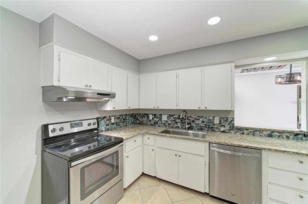 A kitchen with white cabinets, granite countertops, stainless steel appliances, and a blue tile backsplash — 2224 BAHIA VISTA STREET UNIT E6, SARASOTA, FL