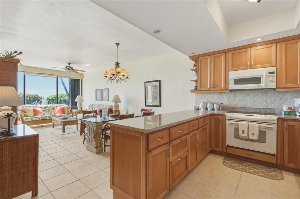 A kitchen with wood cabinets and granite countertops overlooks an open-concept dining and living area — 96 BEACH VILLAGE DRIVE UNIT 96, HUMACAO, PR