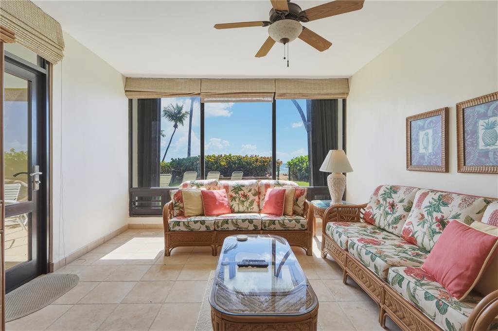 A sunroom features wicker furniture, tile flooring, and large windows overlooking a beach and palm trees — 96 BEACH VILLAGE DRIVE UNIT 96, HUMACAO, PR