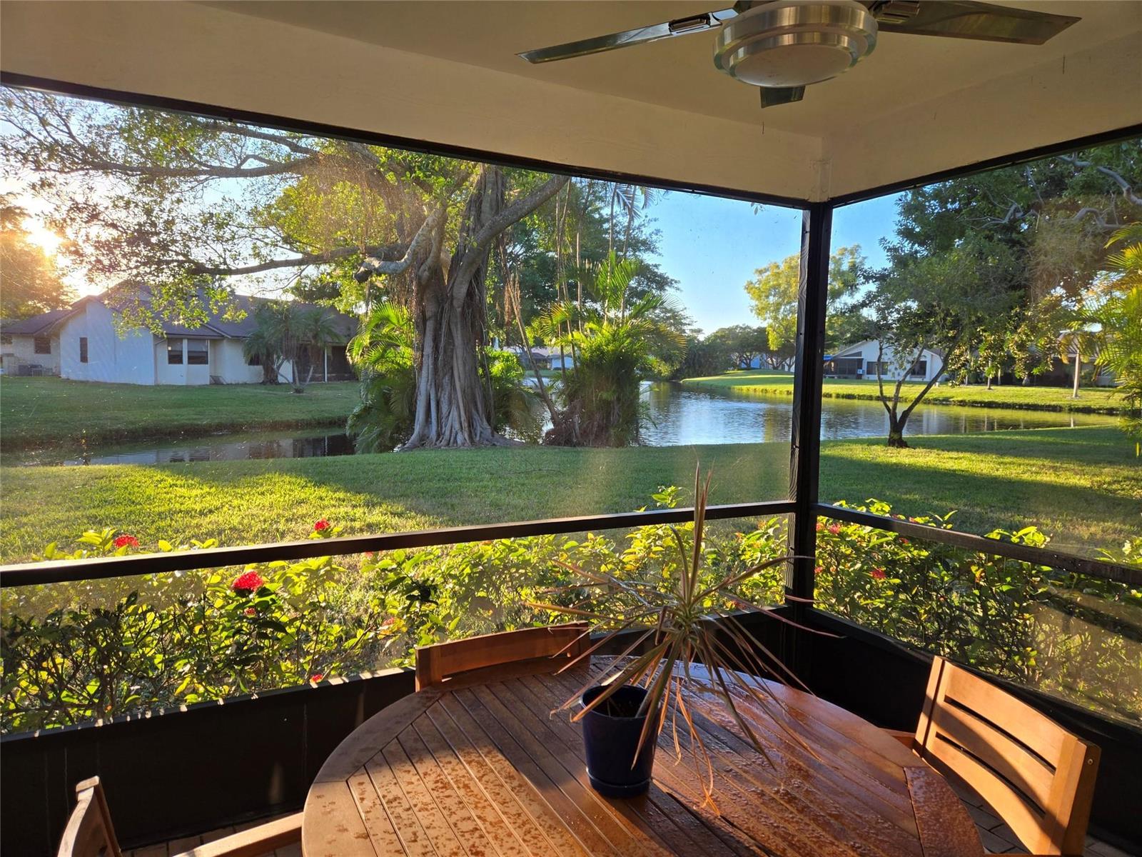 A screened-in patio features a wooden table and chairs overlooking a pond and large trees — 16843 Boca Delray Drive, Delray Beach FL 33484, DELRAY BEACH, FL
