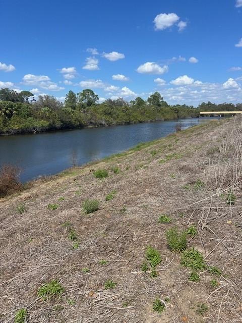 A grassy embankment slopes down toward a canal under a blue sky with clouds — LOT 67 HARCOURT CIRCLE, NORTH PORT, FL