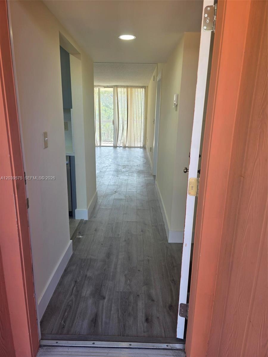 A view through a doorway shows a hallway with wood-look flooring leading to a balcony — 10985 SW 107th St # 312, Miami FL 33176, MIAMI, FL